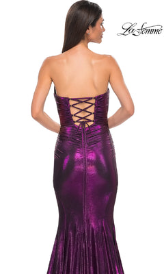 A woman stands with her back to the camera wearing the La Femme 32995 strapless long metallic purple prom dress with a lace-up back; the La Femme logo appears in the upper right corner.