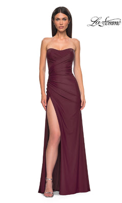 A woman models the La Femme 33012 long prom dress in burgundy, featuring a strapless ruched bodice and high side slit, against a white background.