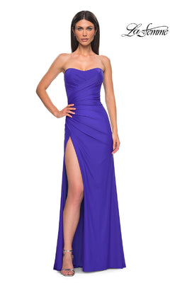A woman poses confidently in the La Femme 33012 long prom dress—sleek, strapless, and royal blue—with a floor-length skirt, thigh-high slit, and elegant ruched detailing.