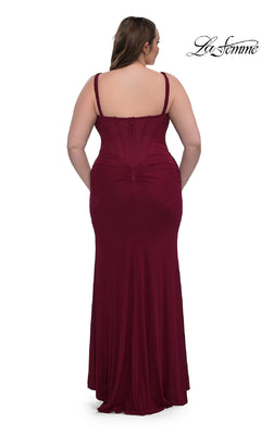 A woman wears the La Femme 33015, a plus-size long corset prom dress in burgundy with ruched back detail. The sleeveless, floor-length fitted formal dress is shown from behind against a white background.
