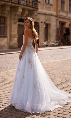 A woman wearing the Strapless Beaded Long Prom Gown La Femme 33028 stands on a cobblestone street, looking over her shoulder.