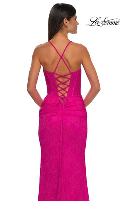 Woman in La Femme 33036 Long Stretch-Lace Prom Dress, bright pink with crisscross straps and lace-up back detail, seen from behind. Signature La Femme logo displayed in the top right corner.
