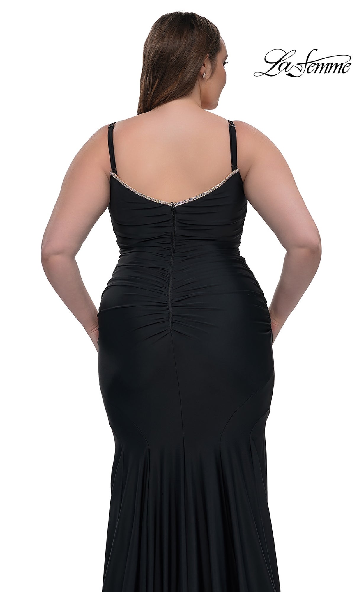 A woman is seen from the back in a fitted black plus-size La Femme 33057 floor-length prom dress with thin straps and ruched details. She stands against a plain white background, with 