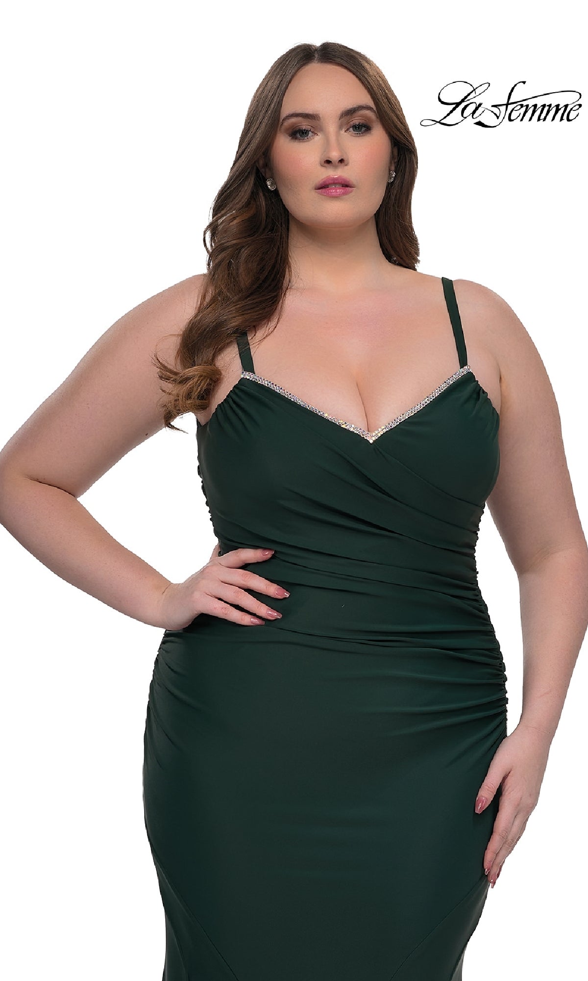 A woman wears the La Femme 33057 plus-size, floor-length prom dress in dark green with a sleeveless fitted design and rhinestone-trimmed neckline, standing against a white background. The La Femme logo is in the upper right corner.