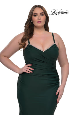 A woman wears the La Femme 33057 plus-size, floor-length prom dress in dark green with a sleeveless fitted design and rhinestone-trimmed neckline, standing against a white background. The La Femme logo is in the upper right corner.