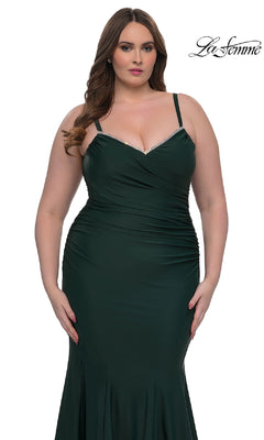 A woman wears the fitted dark green La Femme 33057 plus-size floor-length prom dress with thin straps and ruched details. She stands against a white background with "La Femme" in the top right corner.