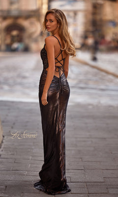 Woman standing on a cobblestone street in the Strappy Long Metallic Prom Dress: La Femme 33059, featuring a lace-up back, looking over her shoulder.