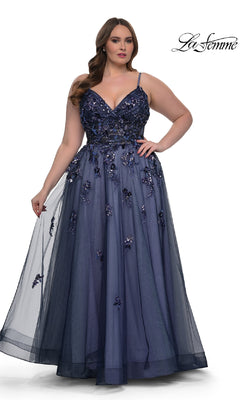 A woman wearing the Navy Plus-Size Prom Dress: La Femme 33061, featuring a floor-length A-line skirt, sequin beaded floral applique, and spaghetti straps, stands while holding out part of the elegant skirt.