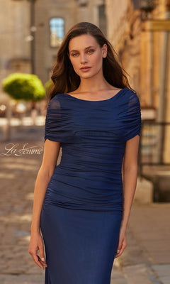 A woman in the La Femme 33139 long formal dress poses outdoors on a cobblestone street, with buildings and greenery in the background.