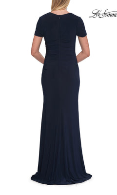A woman is seen from the back wearing the La Femme 33146 Short Sleeve Long Jersey Formal Dress in navy blue. This formal dress showcases subtle ruching at the waist and a fitted, floor-length silhouette.