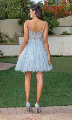 A woman faces away outdoors on grass and pavement, wearing the Short Babydoll Homecoming Dress with Beading in light blue and silver heels.