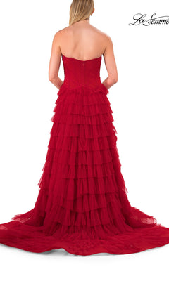 A woman in a La Femme 33202 Strapless Ruffle Prom Ball Gown with layered tulle ruffles stands facing away from the camera against a white background.