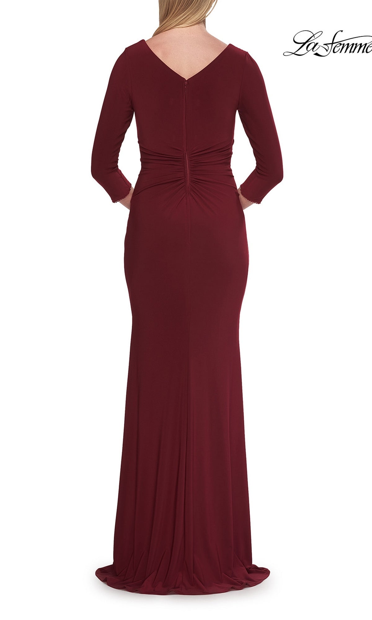 A woman is photographed from the back wearing the La Femme 33214 Long Sleeve Jersey Formal Gown, a floor-length burgundy dress with long sleeves, a V-back, and ruched detailing.