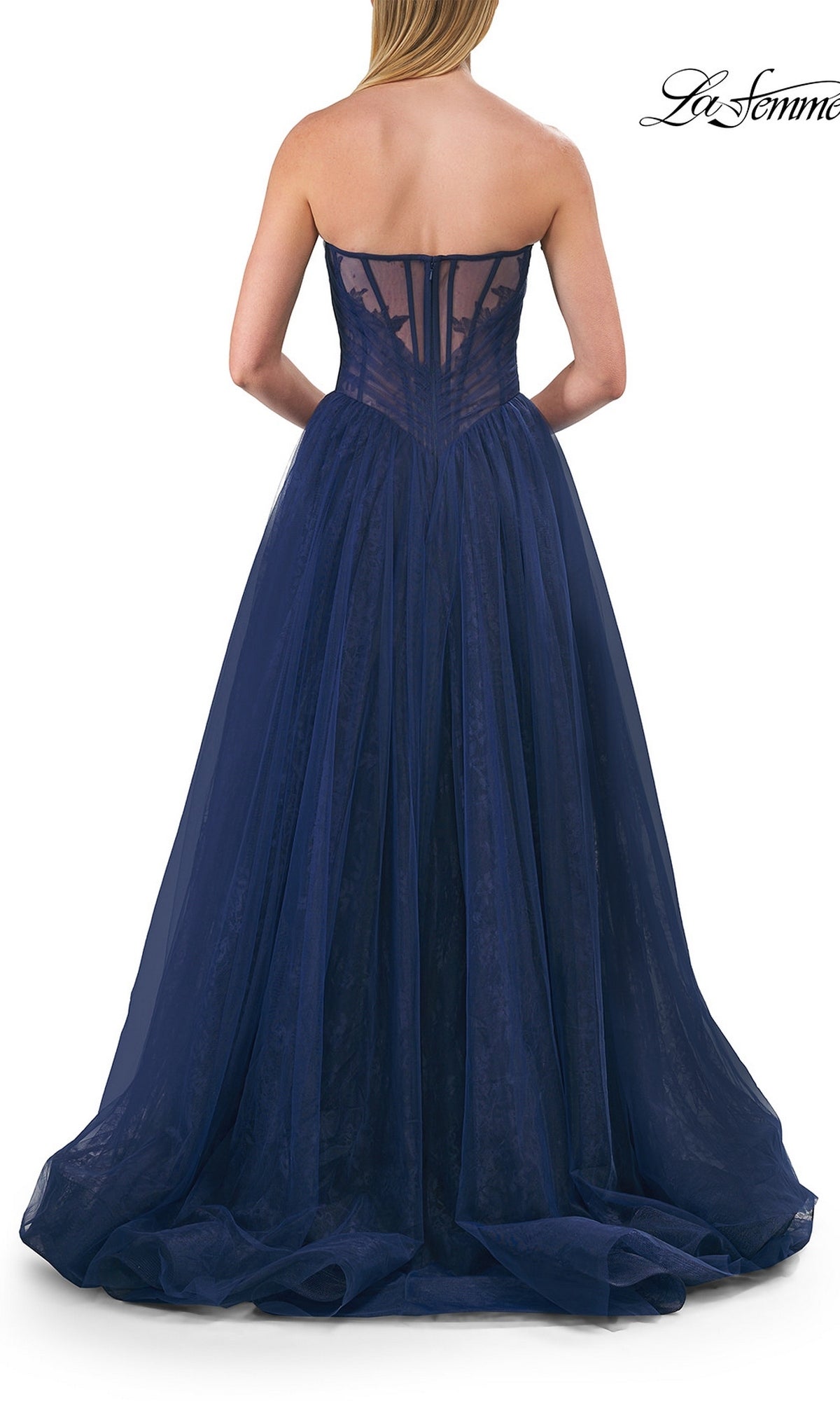 A woman wearing the La Femme 33307 long prom dress in strapless navy blue tulle with a sheer corset back, stands facing away from the camera.