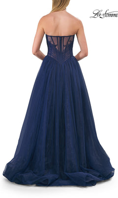 A woman wearing the La Femme 33307 long prom dress in strapless navy blue tulle with a sheer corset back, stands facing away from the camera.