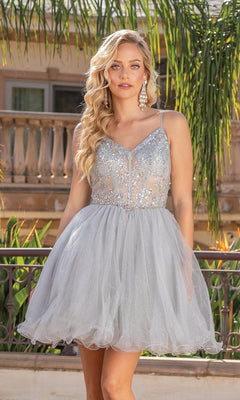 A woman with long, wavy blonde hair and dangling earrings stands outdoors in the Sheer-Corset Short Babydoll Homecoming Dress 3337, featuring a silver glittery a-line shape, thin straps, and a tulle skirt.