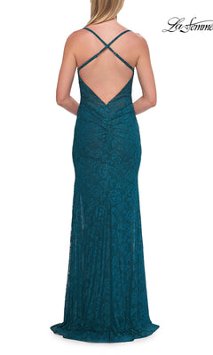 A woman stands facing away from the camera, wearing the La Femme 33381 long prom dress—an elegant floor-length teal lace gown featuring a fitted silhouette, open back, and crisscross straps.
