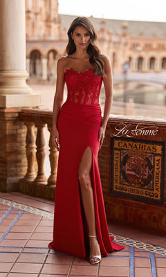 A woman in a red Lace-Corset Strapless Prom Gown (La Femme 33399) with a sweetheart neckline, sheer lace corset, and thigh-high slit stands on a tiled terrace framed by columns and arches.