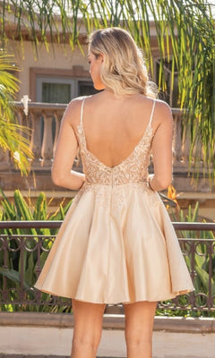 Woman wearing a champagne dress with an open back, standing outdoors with greenery in the background.