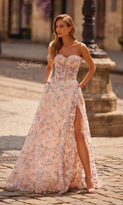 A woman outdoors on a cobblestone street wears the La Femme 33409 long prom dress in multi, featuring a strapless sweetheart neckline, floral design, thigh-high slit, and sheer bodice.