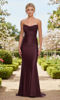 A woman stands outdoors on a garden path wearing the Strapless Ruched Tight Prom Gown La Femme 33415 in wine, featuring a fitted ruched bodice and floor-length design.