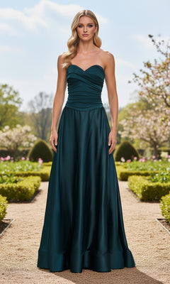 A woman wears the Strapless Sweetheart Prom Gown: La Femme 33417 while standing on a garden path, surrounded by trimmed hedges and blooming trees beneath a clear sky.