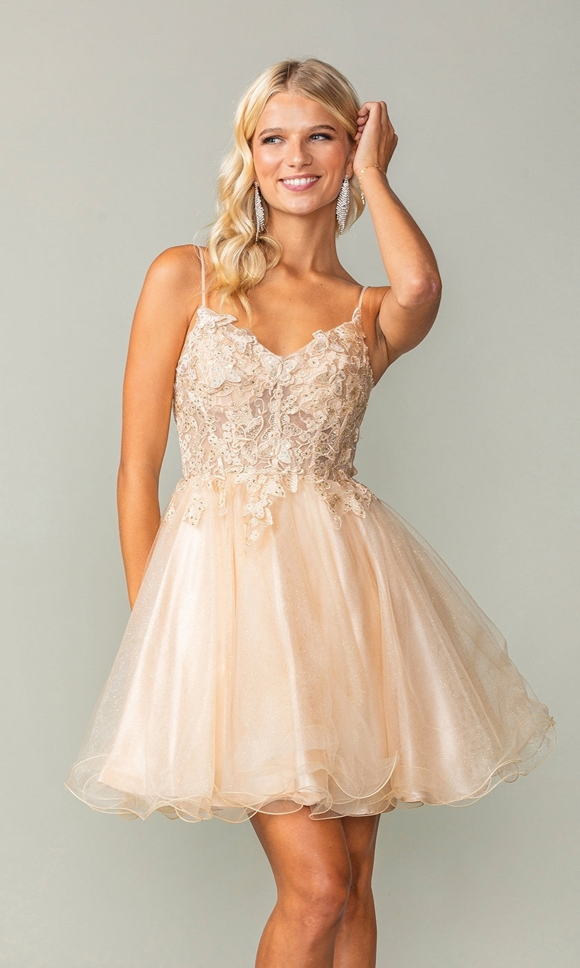 A woman wears the Lace-Up Short Butterfly Homecoming Dress 3341, a sleeveless light peach babydoll dress with lace and tulle, thin straps, and smiles against a plain backdrop.