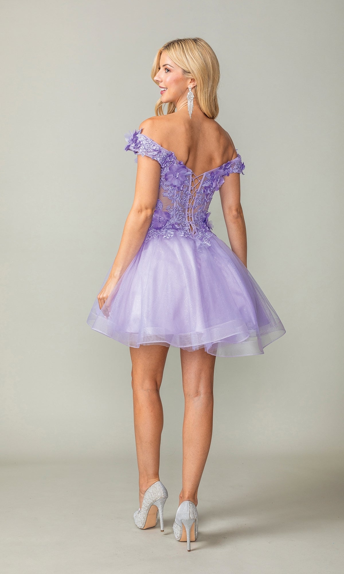 A woman faces away, wearing the Off-the-Shoulder Short Babydoll Hoco Dress 3344 in lavender with floral appliques, a lace-up back, and silver heels.