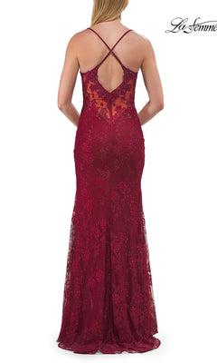 A woman stands facing away from the camera, wearing the La Femme 33473 Long Beaded Floral Lace Prom Dress—a sleeveless, floor-length red gown adorned with floral lace and sequin accents, featuring a low back with crisscross straps.