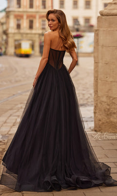 A woman wearing the La Femme 33491 long prom dress with a strapless corset bodice and tulle a-line skirt stands on a cobblestone street, glancing over her shoulder with city buildings in the background.