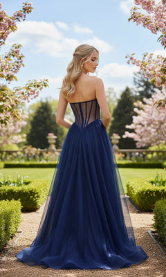 A woman in the Strapless Sheer-Corset Prom Gown: La Femme 33491 stands on a garden path, facing away and surrounded by blooming trees and manicured hedges.