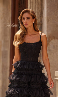 A woman with long blonde hair wears the Long Prom Dress: La Femme 33493, a black sleeveless gown with a tiered ruffle skirt, standing outdoors by an old stone building. "La Femme" is visible in the image.