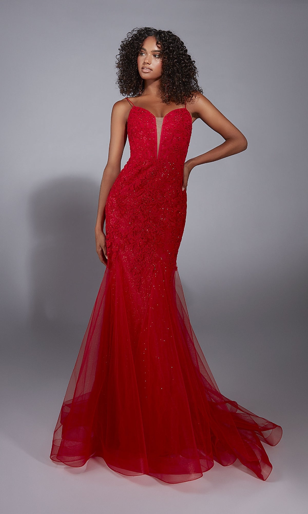 A woman with curly hair models the Aerie Couture 334 Long Prom Dress—a fitted, floor-length red mermaid gown with thin straps, open back, and sheer tulle skirt—against a plain gray background.