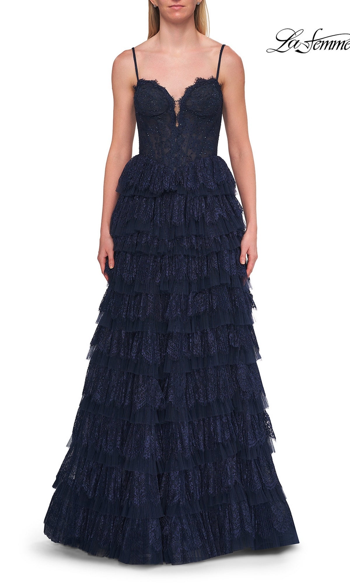 A woman models the La Femme 33525 Long Prom Dress—a navy blue, sleeveless evening gown featuring a fitted corset bodice and tiered ruffle skirt—while standing against a white background.