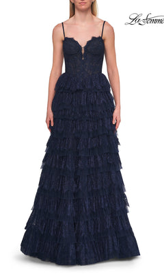 A woman models the La Femme 33525 Long Prom Dress—a navy blue, sleeveless evening gown featuring a fitted corset bodice and tiered ruffle skirt—while standing against a white background.