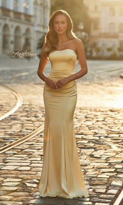 A woman in the La Femme 33546 long prom dress, a strapless and fitted style in pale yellow satin, stands on a cobblestone street in natural sunlight.