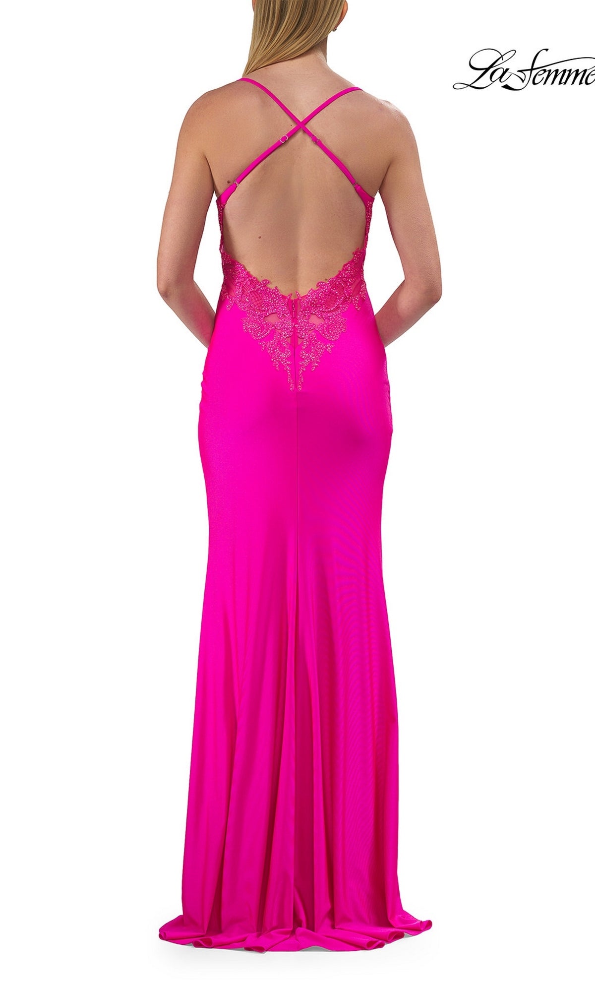A woman wearing the La Femme 33553 cowl-neck strappy long prom dress in bright pink, featuring lace details and a crisscross strappy-back design, stands with her back to the camera.