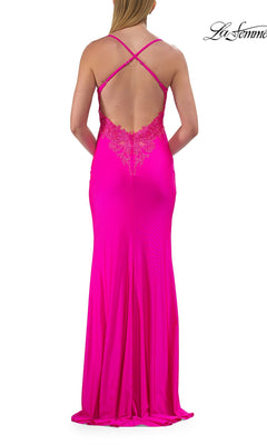 A woman wearing the La Femme 33553 cowl-neck strappy long prom dress in bright pink, featuring lace details and a crisscross strappy-back design, stands with her back to the camera.
