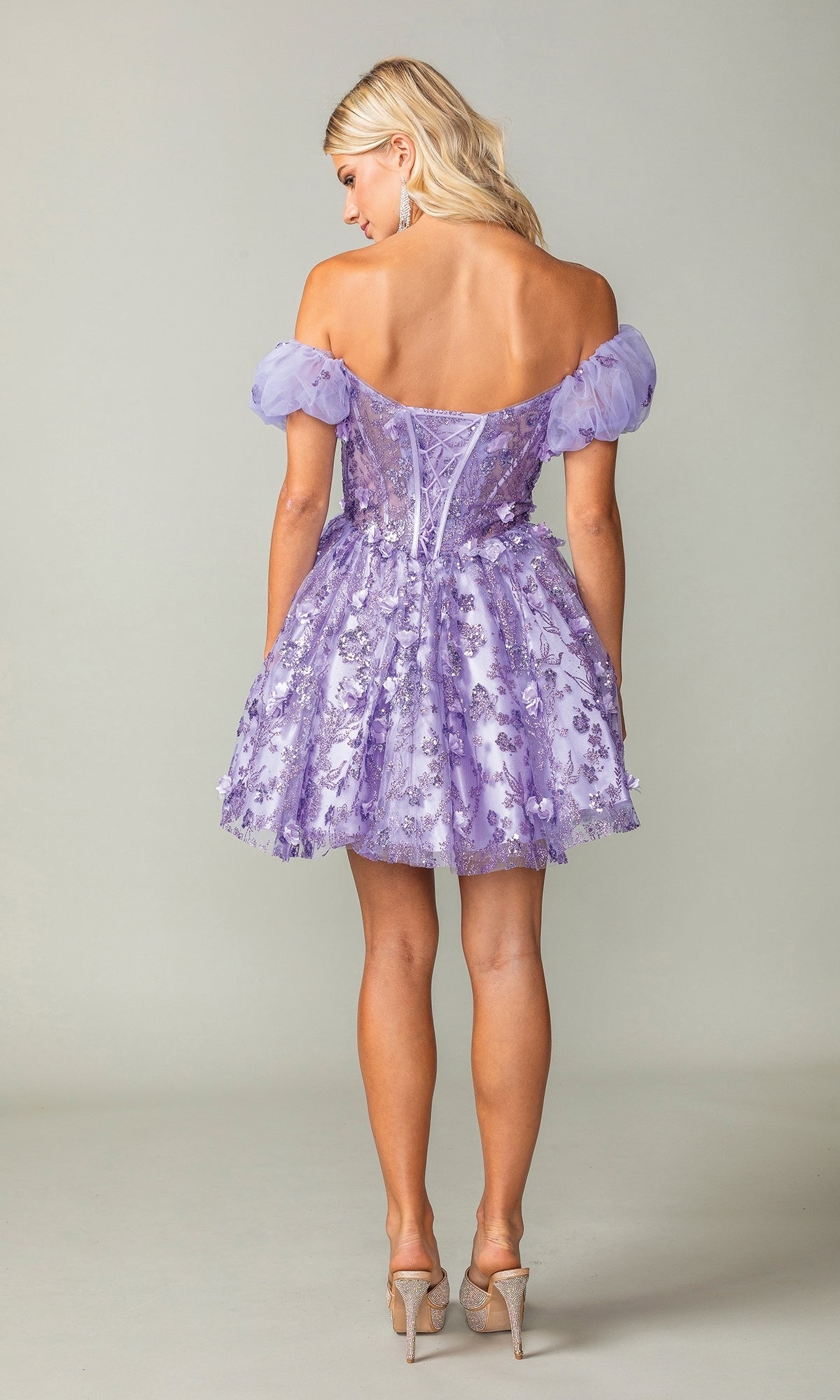 A woman stands facing away, wearing the Short Sleeve Short Glitter Homecoming Dress 3355 with puff sleeves and clear high heels.