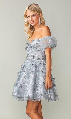 A woman wears the Short Sleeve Short Glitter Homecoming Dress 3355, a silver mini dress with puff sleeves and glitter detail, posing against a plain light background.
