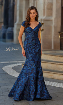 A woman stands outdoors on a stone walkway near building steps, wearing the La Femme 33578 long formal dress in navy—a fitted, floor-length mermaid gown with cap sleeves.