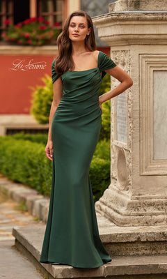 A woman stands outdoors in the La Femme 33584 long formal dress, featuring a fitted dark emerald design with off-the-shoulder straps and flattering ruching, next to a stone monument.