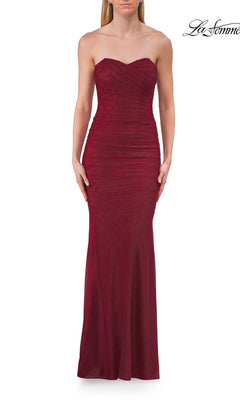 A woman wearing the Classic Strapless Long Prom Dress La Femme 33601—a floor-length, fitted raspberry gown with ruched detailing and subtle embellishments—stands against a white background.