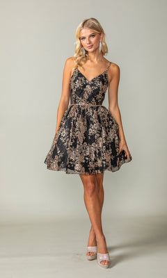 A woman wears the Short A-Line Glitter-Print Homecoming Dress 3360—sleeveless, black with gold floral patterns—paired with silver open-toe heels and dangly earrings, standing against a plain light gray background.