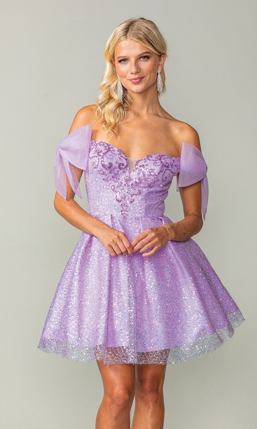 A woman models the Shoulder-Bow Short Glitter Homecoming Dress 3363, featuring off-the-shoulder tulle bows, sparkling sequins, and a corset lace-up back, as she stands against a plain background.