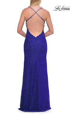 A woman stands facing away from the camera in the Beaded Long Lace Prom Dress: La Femme 33647, a floor-length, royal blue gown featuring delicate beaded lace, thin crisscross straps, and a low open back.