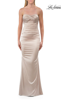 A woman wearing the La Femme 33654 lace-up strapless long prom dress in champagne, featuring a body-contouring floor-length gown with ruched bodice detail, stands against a white background.
