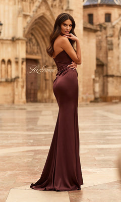 A woman wears the La Femme 33670 long prom dress with a ruched bodice, standing outdoors on stone pavement with historic architecture in the background.