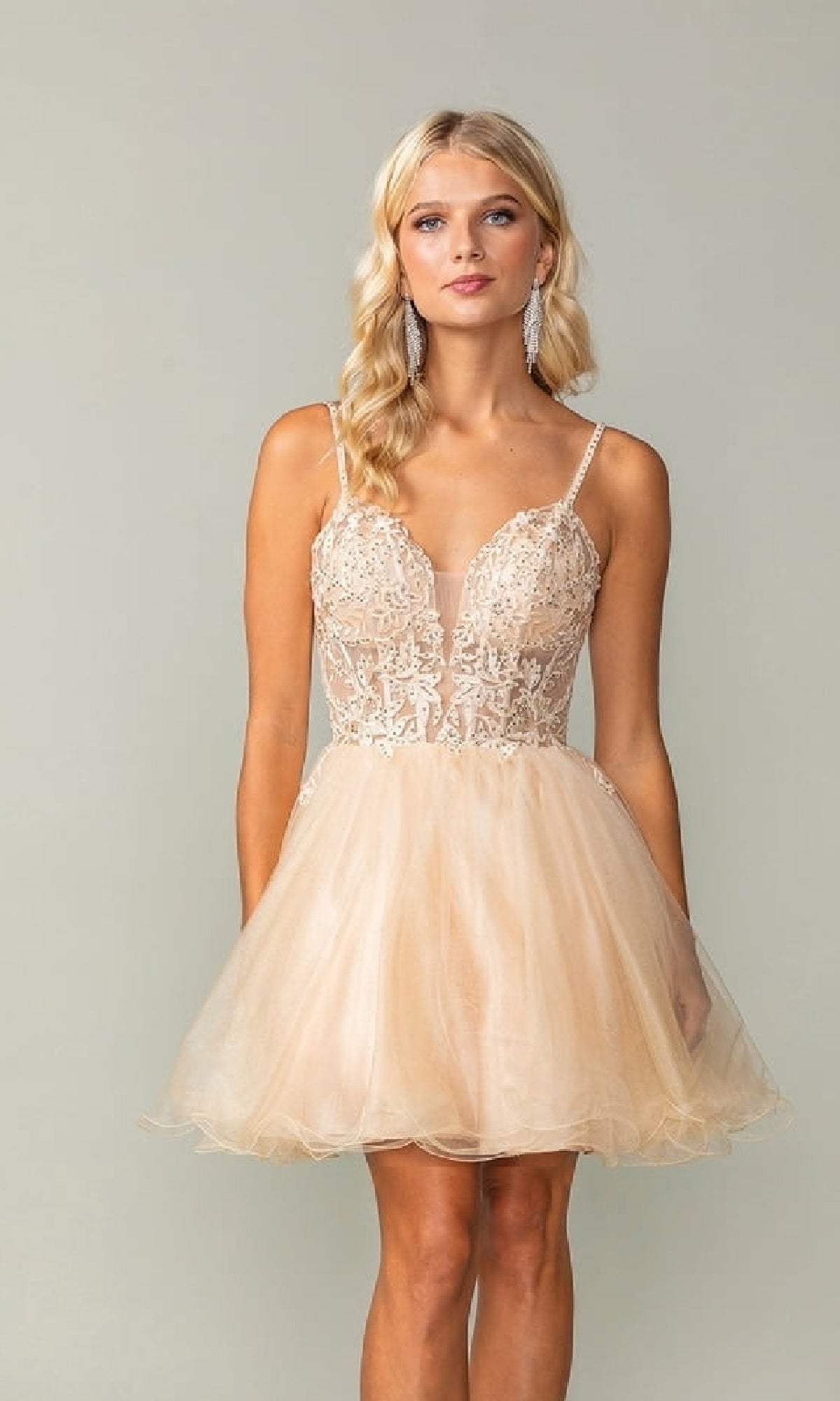 Woman wearing a champagne colored short dress against a plain background