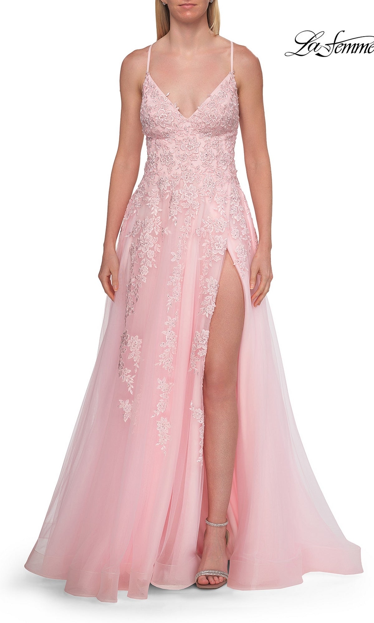 A woman wears the La Femme 33715 Floral Lace Embroidered Prom Dress in baby pink, featuring a sleeveless design, spaghetti straps, and a high slit, paired with neutral heels against a white background.